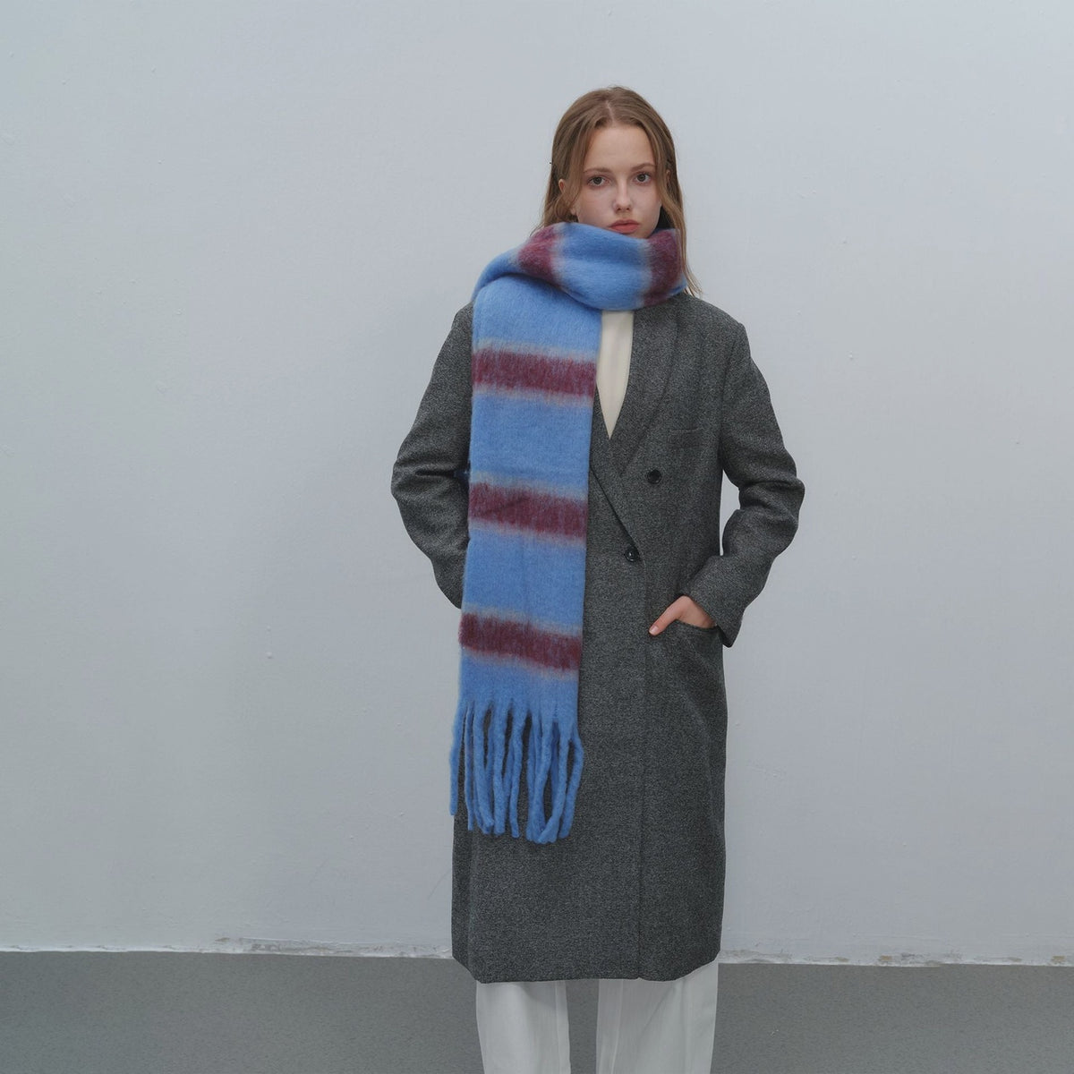 Blue and burgundy striped fuzzy mohair scarf with fringe ends, shown styled over a gray wool overcoat.