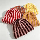 Four ribbed knit striped beanies in red/white, orange/blue, yellow/pink, and brown/pink colorways with cuffed brims.