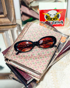 Sunglasses on top of a stack of books with a visible brand logo in the background.