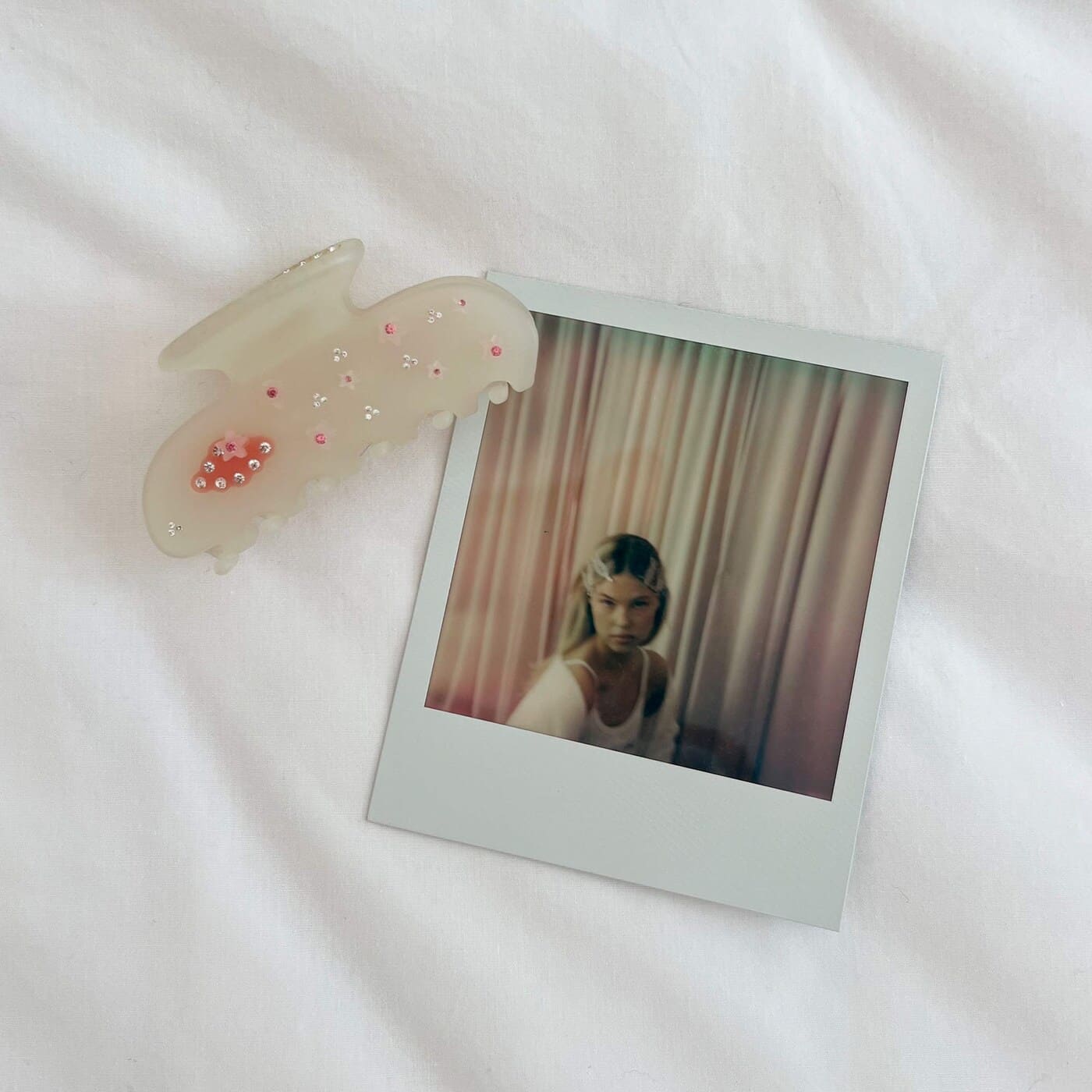 Translucent white butterfly hair claw clip with pink and clear crystal embellishments on white fabric background