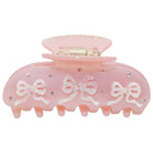 Pink plastic hair claw clip with white bow designs and clear rhinestone embellishments on a spring-loaded clasp