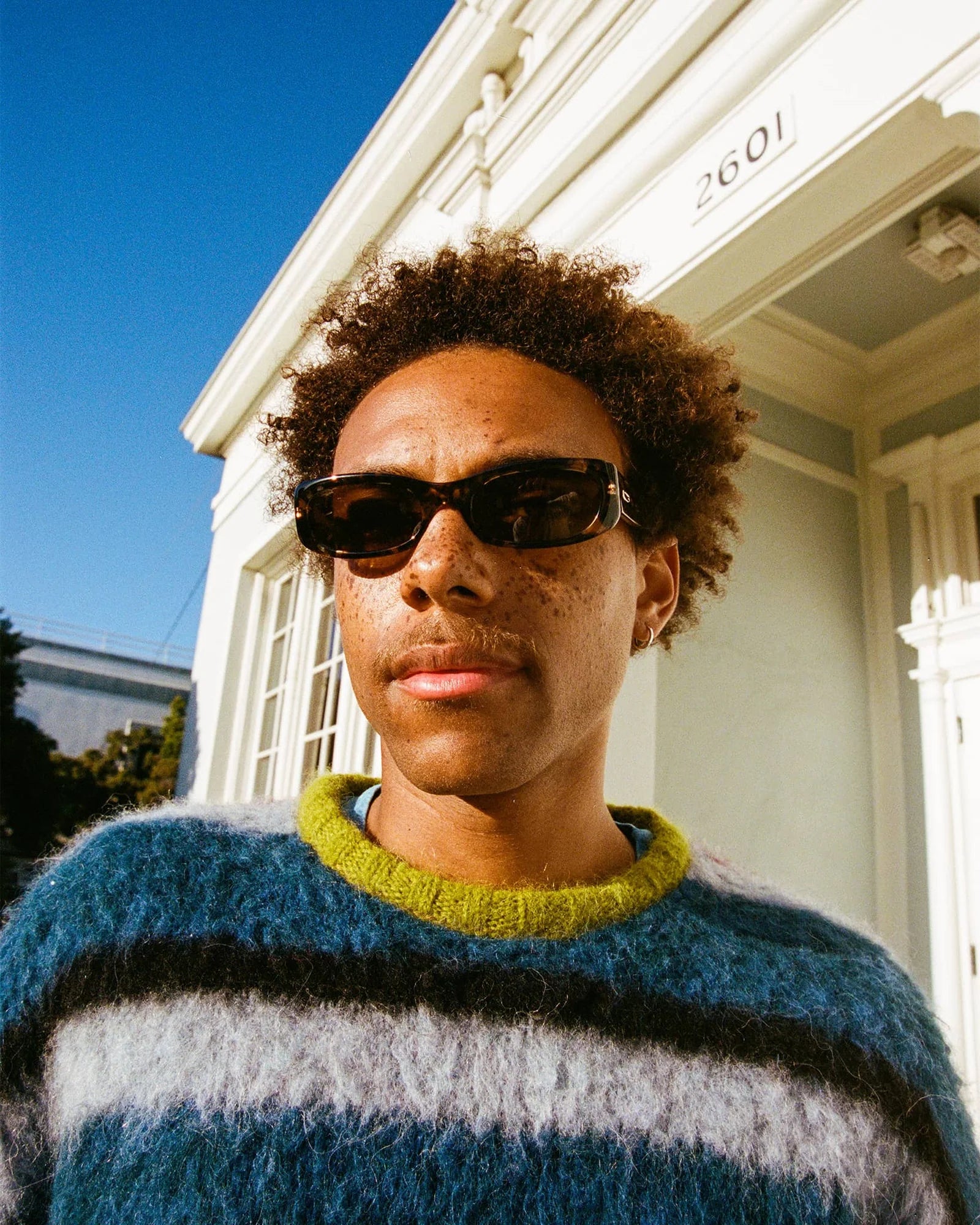 Person wearing sunglasses and a striped sweater in front of a white building